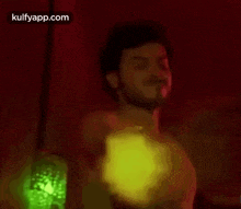 a shirtless man is dancing in a dark room with a green lamp in the background .