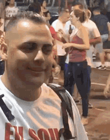 a man is smiling while standing in front of a crowd of people on a street .