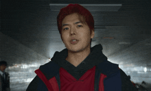 a young man with red hair and a red vest is pointing at the camera