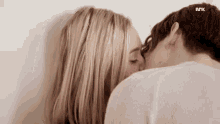 a man and a woman are kissing each other against a white wall .