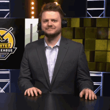 a man in a suit and headphones stands in front of a screen that says elite 7 league