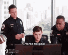 a group of police officers are standing around a man sitting in front of a computer screen ..