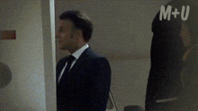 a man in a suit and tie is standing in a doorway with m + u on his back