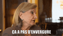 a woman is sitting at a table with the words ca a pas d' envergure written on her face