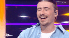 a man in a blue shirt is laughing with his eyes closed