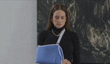 a woman with a blue arm sling is wearing a black turtleneck