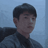a young man in a suit and tie is sitting in a chair and looking at the camera .