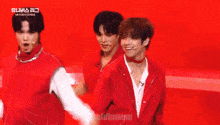 a group of young men in red jackets are dancing on a stage