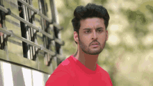 a man with a beard wearing a red shirt looks at the camera