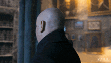 a bald man is standing in front of a wall with a netflix logo on the bottom