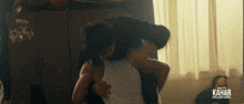 a man is carrying another man in his arms with the word kahar on the bottom right