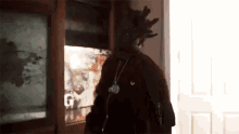 a man with dreadlocks and a necklace is standing in a doorway .