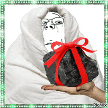 a picture of a person wrapped in a blanket holding a rock tied with a red ribbon