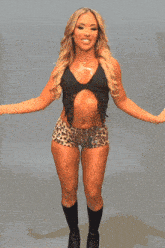 a woman in a black top and leopard print shorts stands in front of a lizard