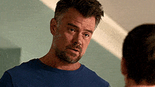 a man with a beard is wearing a blue shirt and looking at another man .