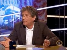 a man in a suit is sitting at a table with the number 12 in the corner