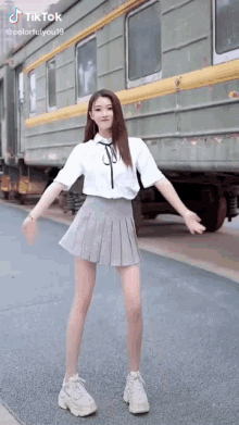 a girl in a white shirt and gray pleated skirt is standing in front of a train .