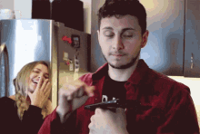 a man in a red jacket is holding a gun while a woman laughs