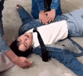 a man in a denim jacket and tie is laying on the floor with his hands on his chest .