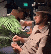 a man in a hat is smoking a cigarette while drinking from a cup .