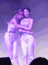 two women hugging each other on a stage with purple lights behind them