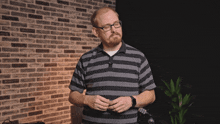 a man with glasses and a striped shirt is standing in front of a brick wall