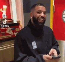 a man with a beard is standing in front of a red door holding a cell phone .