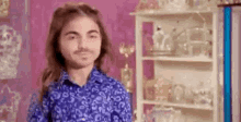 a young man with long hair and a beard is standing in front of a shelf filled with vases .