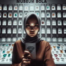 a woman in a hijab is holding a diamond card in front of a wall that says " museum bola "