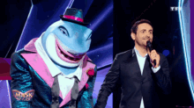a man in a suit stands next to a masked singer shark