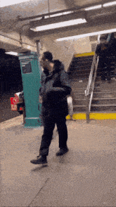 a man in a black jacket is walking down stairs at a subway station