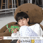 a young man is sitting in a chair with a teddy bear on his head and holding a toy .