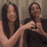 two women making a heart shape with their hands