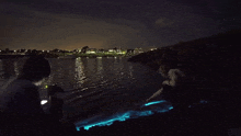 a couple of people standing on the shore of a body of water at night