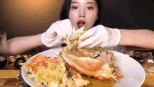 a woman in white gloves is eating a large crab on a white plate .
