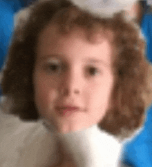 a little girl with curly hair is wearing a white hat and holding a white stuffed animal .