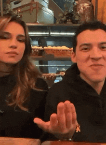 a man and a woman are sitting at a table in a restaurant . the man is making a funny face .