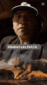 a man wearing a hat is holding a dog with the words günbatimi fatih written on the bottom