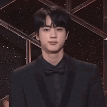 a man in a black suit and bow tie looks at the camera