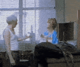 a man in a white tank top is talking to a woman in a blue dress