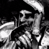 a black and white photo of a knight in armor holding a sword .