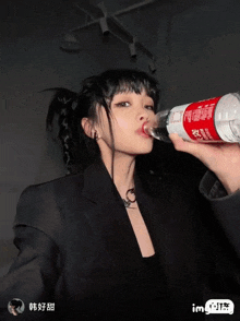 a woman in a black suit holds a bottle of water with chinese writing on it