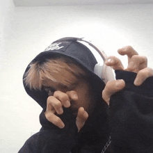 a person wearing a hoodie and headphones is covering their face with their hands .