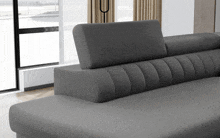 a grey couch in a living room with a window behind it