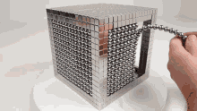 a person is holding a string of metal balls in front of a cube