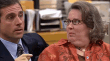 a man in a suit and tie is sitting next to a woman in a red shirt .