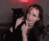 a woman with pink hair is holding a black cat in front of a microphone