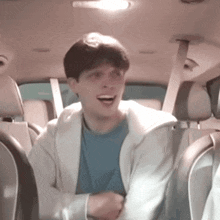 a man wearing a blue shirt and a white hoodie is sitting in the back seat of a car
