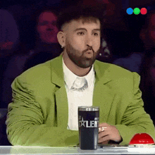 a man in a green suit holds a cup that says talent on it