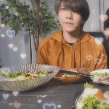 a young man sits at a table with plates of food and hearts around him